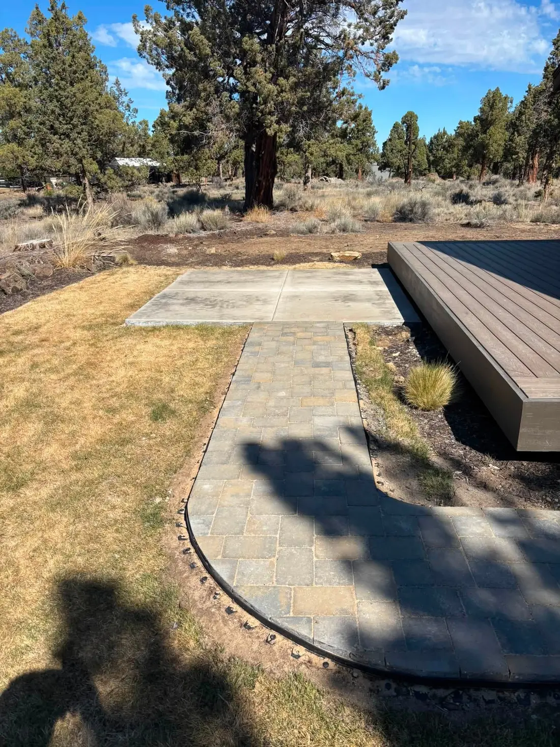 Concrete pad and curved paver walkway beside a composite deck