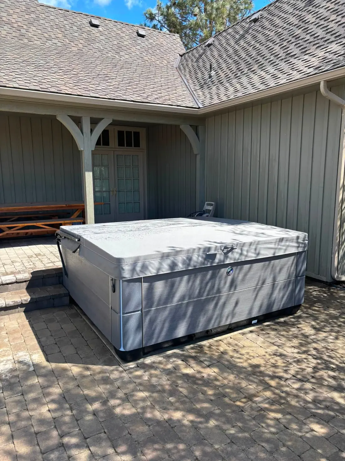 Hot tub set on a paver patio beside a covered porch